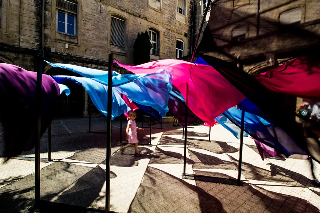 Photo d'une petite floue qui marche entre des voiles roses et bleus pour le festival Architectures Vives"