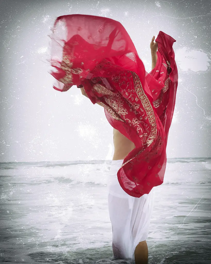 photo d'une femme qui tient un grand foulard ou un paréo fuchsia face à la mer